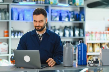 Üniformalı bir adam oto yedek parça mağazasında dizüstü bilgisayar kullanıyor, ürünleri tarıyor ve malları yönetiyor.
