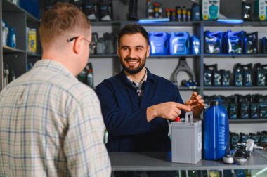 Bir otomotiv mağazasında bir müşteriye araba aküsü ve diğer araç parçalarını seçmesinde yardımcı olan satıcı