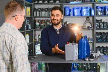 Gülümseyen mekanik danışman müşteri araba aküsü ve motor yağı hakkında, otomotiv hizmeti ve bakım çözümleri sunuyor