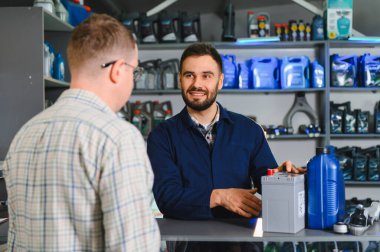 Otomobil parçaları satıcısı, erkek müşteriye yeni bir araç aküsü seçmesini, kalite seçenekleri ve yedek ürünleri göstermesini tavsiye ediyor