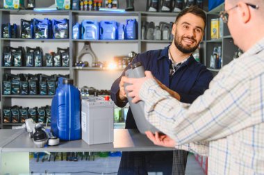 Gülümseyen otomobil parçaları mağazası çalışanı müşteriye motor yağı sunuyor, iyi hizmet ve araç bakım ürünleri sergiliyor