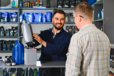 Otomobil tamircisi, bir perakende mağazasında uzman tavsiyesi vererek, müşteriye oto bakımı için yağ ve pil seçmesinde yardımcı oluyor.
