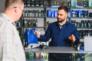 Çalışan, perakende oto yedek parça mağazasında çalışan bir erkek müşteriye motor yağı ve araba parçaları konusunda yardım ederek,
