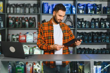 Ekose gömlekli genç bir adam otomotiv mağazasında hisse senetlerini gözden geçiriyor, araba bakım malzemelerini yönetiyor.