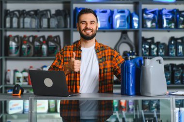 Bir oto yedek parça mağazasında çalışan, gülümseyen ve baş parmağını kaldıran, motor yağıyla tezgahın arkasında duran bir adam.