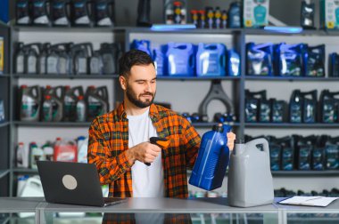 Bir oto yedek parça mağazasında, envanter ve satışları yöneten barkod okuyucusu kullanarak motor yağı kutusunu tarayan adam.