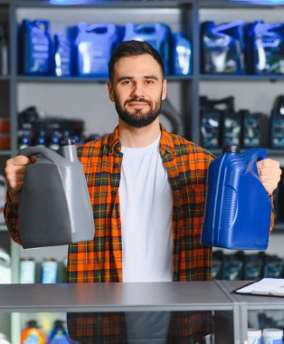 Oto yedek parça mağazasında çalışan adam iki şişe motor yağı tutuyor ve araba motoru bakımı için seçenekler sunuyor.