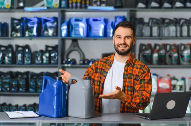 Gülümseyen adam otomotiv parçaları dükkanında duruyor, kayganlaştırıcı şişeler tutuyor ve müşterilere araba bakım ürünleri sunuyor.