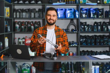 Bir otomotiv parçası mağazasında kolunda süspansiyon koluyla gülümseyen bir işçi, araba yedek parçalarını gösteriyor ve servis sunuyor.