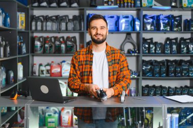 Tezgahın arkasında elinde otomotiv parçası tutan dost canlısı bir erkek satıcı. Raflar araba yağı ve arka planda sıvılarla dolu