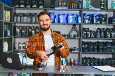 Bir oto yedek parça mağazasında çalışan gülümseyen erkek satıcı, araba süspansiyon bileşenlerini tutuyor ve müşterilere yardım etmeye hazır.