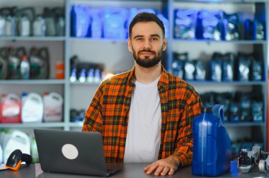 Dizüstü bilgisayarı ve motor yağıyla tezgahın arkasında duran erkek işçi bir otomotiv parçası dükkanında profesyonel hizmet sunuyor.