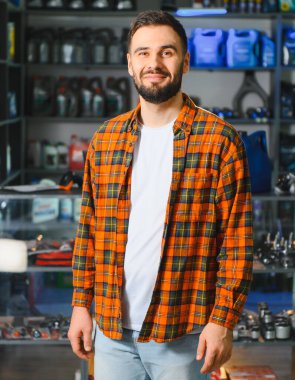 Ekose gömlek ve açık renk kot giyen sakallı bir müşteri otomotiv ürünleri alırken güvenle gülümsüyor.