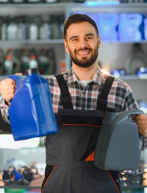 Araba parçası mağazasında gülümseyen servis çalışanı, araba bakımı için iki farklı şişe motor yağı sunuyor.