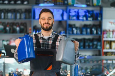 Gülümseyen tamirci ya da tezgahtar elinde iki şişe motor yağı tutarak araç bakımı için yağlama ürünleri sunuyor.