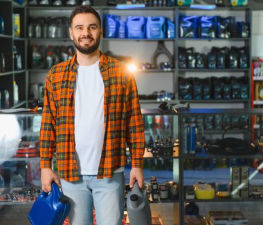 Genç adam araba sıvısı ve bakım malzemeleri alıyor. Perakende dükkanında yağ konteynırları tutan müşteri