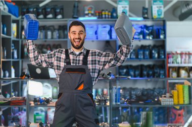 İki motor yağı şişesini elinde tutan mutlu tamirci perakende oto yedek parça mağazasında gülümsüyor.
