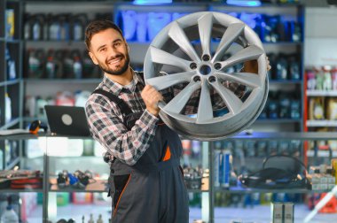 Araba parçaları mağazasında çalışan gülümseyen tamirci, bir alaşım tekerleği tutuyor, profesyonel hizmet ve otomotiv onarımı sunuyor