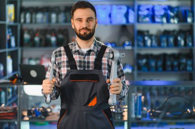 Genç oto tamircisi gülümsüyor, modern araba kontrol kolunu gösteriyor. Bir atölyede ya da oto yedek parça mağazasında durmak