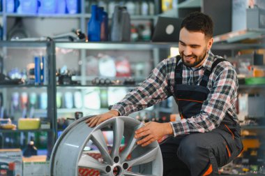 Gülümseyen tamirci lastik dükkanındaki alaşım çarkını kontrol ediyor, araç bakımına ve güvenilir servise odaklanıyor