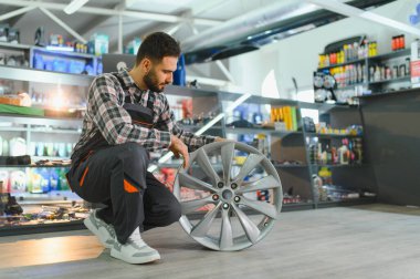 Genç erkek tamirci araba alaşımının kenarını inceliyor, otomotiv servisi ve lastik değiştirme için kalite ve hazırlık sağlıyor