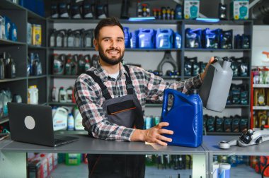 Gülümseyen tamirci ya da satıcı, araba tamirhanesinde ya da perakende oto yedek parça dükkanında çalışırken motor yağı kutularını tutuyor.