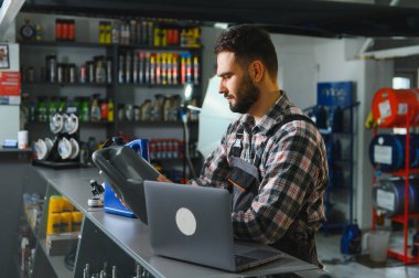Otomobil servis teknisyeni, motor yağı seçimi ve müşteri araç bakımı için dizüstü bilgisayar kullanıyor.