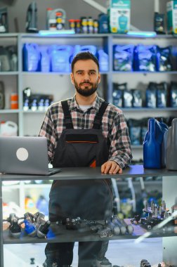 Üniformalı bir adam elinde dizüstü bilgisayar ve kayganlaştırıcı ile bir otomotiv ve perakende mağazasında çalışıyor.