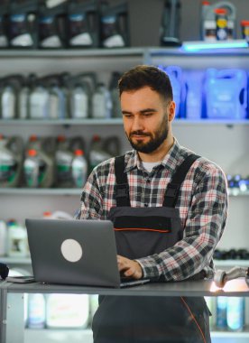 Otomotiv işçisi araba parçaları dükkanında envanteri kontrol ediyor, raflarda ürünlerle tezgahta bekliyor.