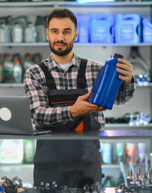 Erkek satıcı veya tamirci bir otomotiv veya parça dükkanında müşteriye bir şişe motor yağı gösteriyor