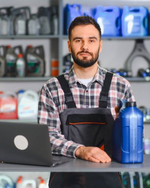 Bir oto yedek parça dükkanında elinde bir şişe motor yağı olan ve dizüstü bilgisayar kullanan bir erkek işçi.