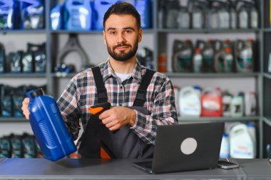 Oto yedek parça mağazası satıcısı bir şişe motor yağını barkod okuyucuyla tarıyor, bilgisayarla tezgahta çalışıyor.