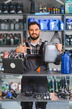 Otomobil parçaları mağazasında duran mutlu tamirci motor yağı konteynırını işaret ediyor. Mükemmel bir araba hizmeti sunuyor.