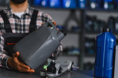 Otomotiv işçisi gri bir teneke kutuda yeni motor yağlayıcısı sunuyor. Araç tamiri ve rutin tamirat için araba parçaları var.