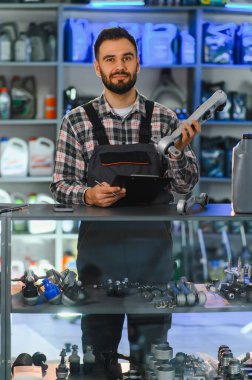 Üniformalı bir adam araba süspansiyon parçası ve dosya tutuyor, oto yedek parça mağazasında ya da garajda çalışıyor, envanteri kontrol ediyor.