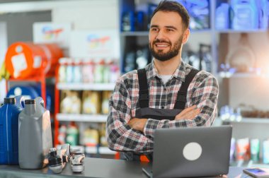 Otomobil parçaları çalışanı, bir dizüstü bilgisayar, motor yağı ve parçaları ile güvenle tezgahta duruyor.