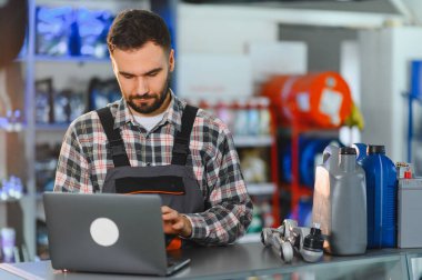Otomobil tamircisi dizüstü bilgisayarda çalışıyor, otomotiv parçaları ve servis tezgahında siparişleri ve envanteri yönetiyor.