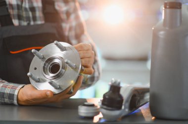 Mekanik, bulanık bir arka planda araba tamiri ve bakımı için yeni bir tekerlek merkezi parçası tutuyor.