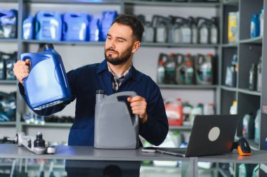 Parça sayacında motor yağı kutuları tutan adam, otomotiv perakende mağazasında araç bakımı için markaları karşılaştırıyor