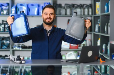 Üniformalı bir adam otomotiv mağazasında farklı motor yağı tiplerini karşılaştırıyor. Araba bakımı için servis ve ürün seçimi sağlanıyor
