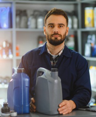 Oto yedek parça mağazasında çalışan genç adam, araba bakımı ve kayganlaştırıcı satışları için motor yağı sunuyor.