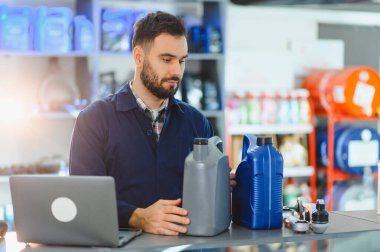 Otomobil teknisyeni motor yağı şişelerini inceliyor ve modern bir garajda dizüstü bilgisayar kullanıyor, envanter ve malzemeleri kontrol ediyor.
