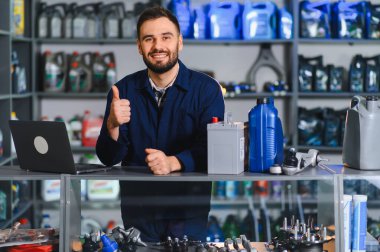 Üniformalı dost canlısı tamirci, araba parçaları ve kayganlaştırıcılarla bir tezgahın önünde dikilip,