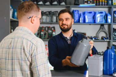 Otomobil parçaları işçisi müşteriye tamir ürünleri seçmesinde yardım ediyor, motor yağı ve pil satıyor.