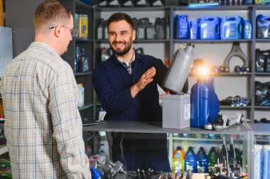 Bir perakende mağazasında müşteriye motor yağı ve araba aküsü hakkında tavsiye veren otomobil parçaları satıcısı, farklı seçenekler sunuyor