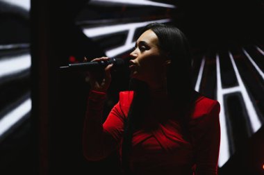 Konser sırasında mikrofon tutan ve şarkı söyleyen kadın vokalist. Dinamik ışıklandırma eğlence için dramatik bir atmosfer yaratıyor