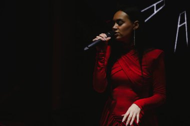 Elinde mikrofon tutan bir kadın vokalist, konser sırasında sahne ışıklarıyla aydınlatılmış bir şarkı söylüyor.