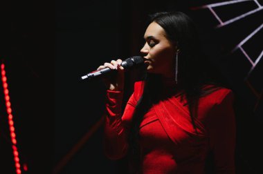 Bir konser performansı sırasında sahnede mikrofon tutan ve canlı vokal yapan kadın şarkıcı