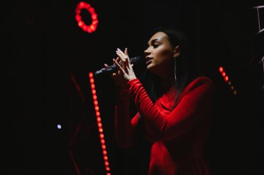 Sahnede kırmızı ışıkların altında şarkı söyleyen kadın vokalist, bir konser veya müzik etkinliğinde sahne alıyor. Tutkulu bir müzik performansına odaklanıyorum.