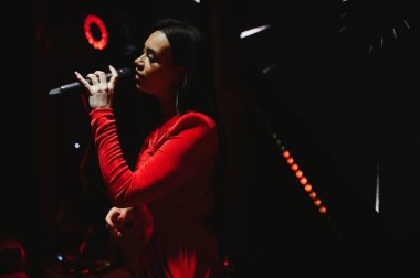 Yetenekli genç bir kadın mikrofona şarkı söylüyor. Karanlık kulüp ışıkları altında büyüleyici bir canlı performans sergiliyor.